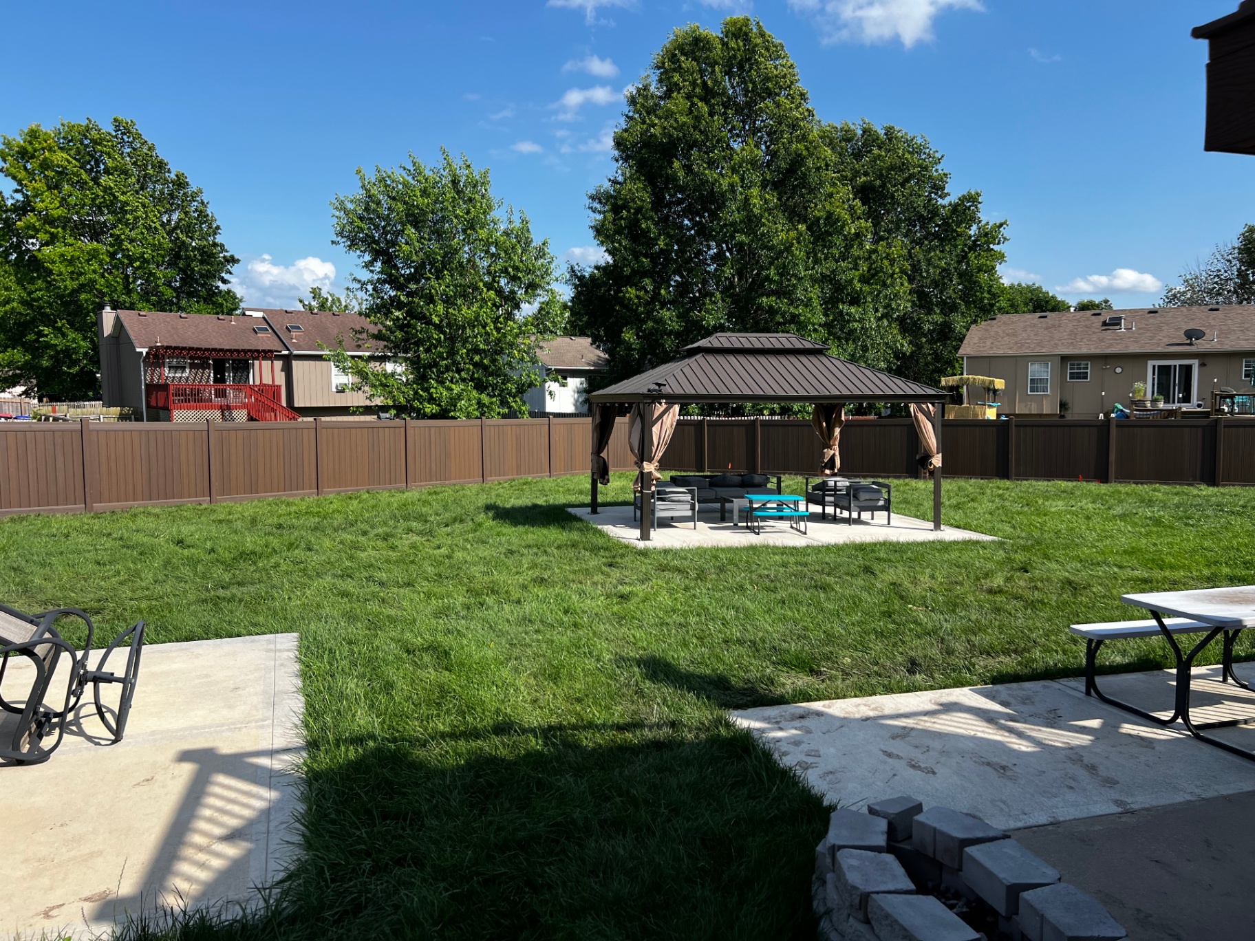 Long run of 6 ft Woodland Select Chestnut brown vinyl privacy fence along a freshly graded backyard with mature trees — Greenwood, MO