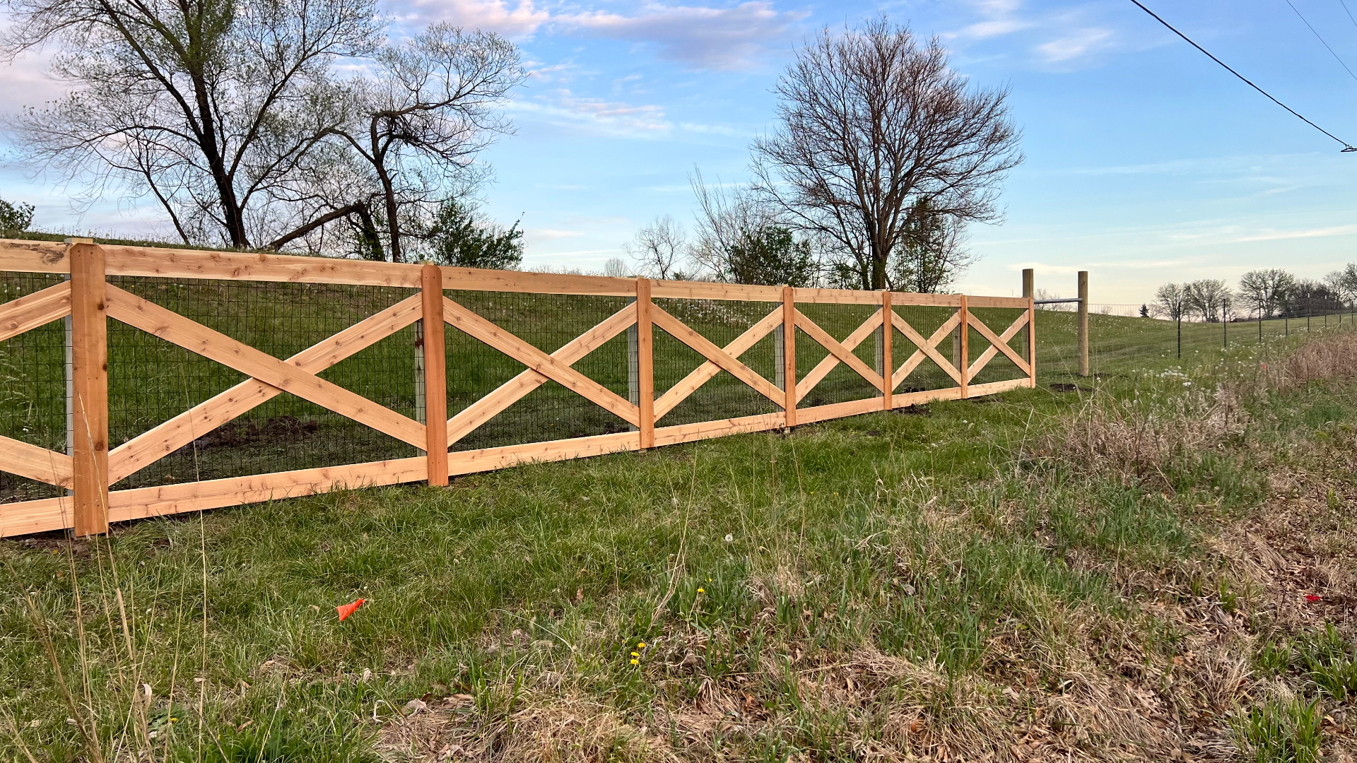 Close view of red cedar cross rail ranch fence backed with Red Brand no-climb welded wire mesh securing a goat pasture — Spring Hill, KS