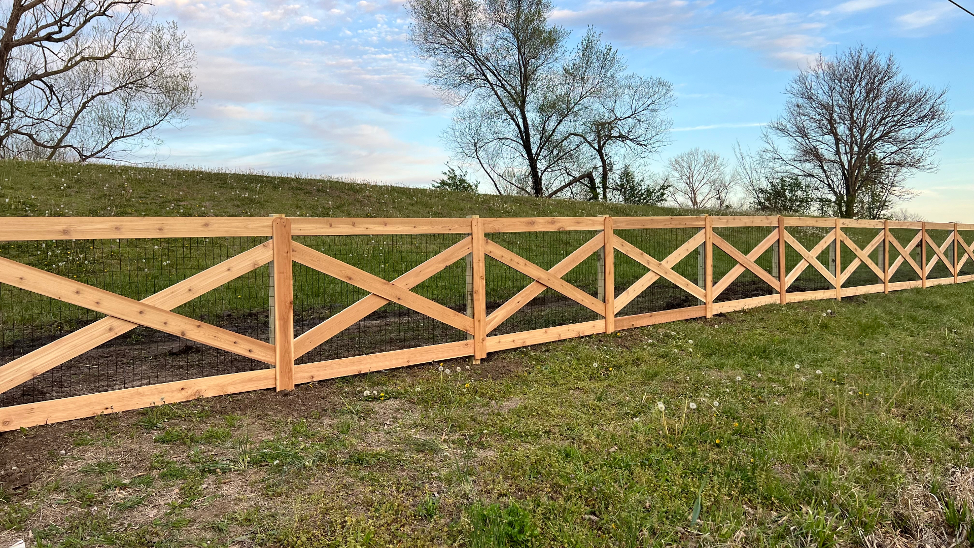 Long run of red cedar cross rail ranch fence with Red Brand no-climb wire mesh along a rolling pasture hillside — Spring Hill, KS