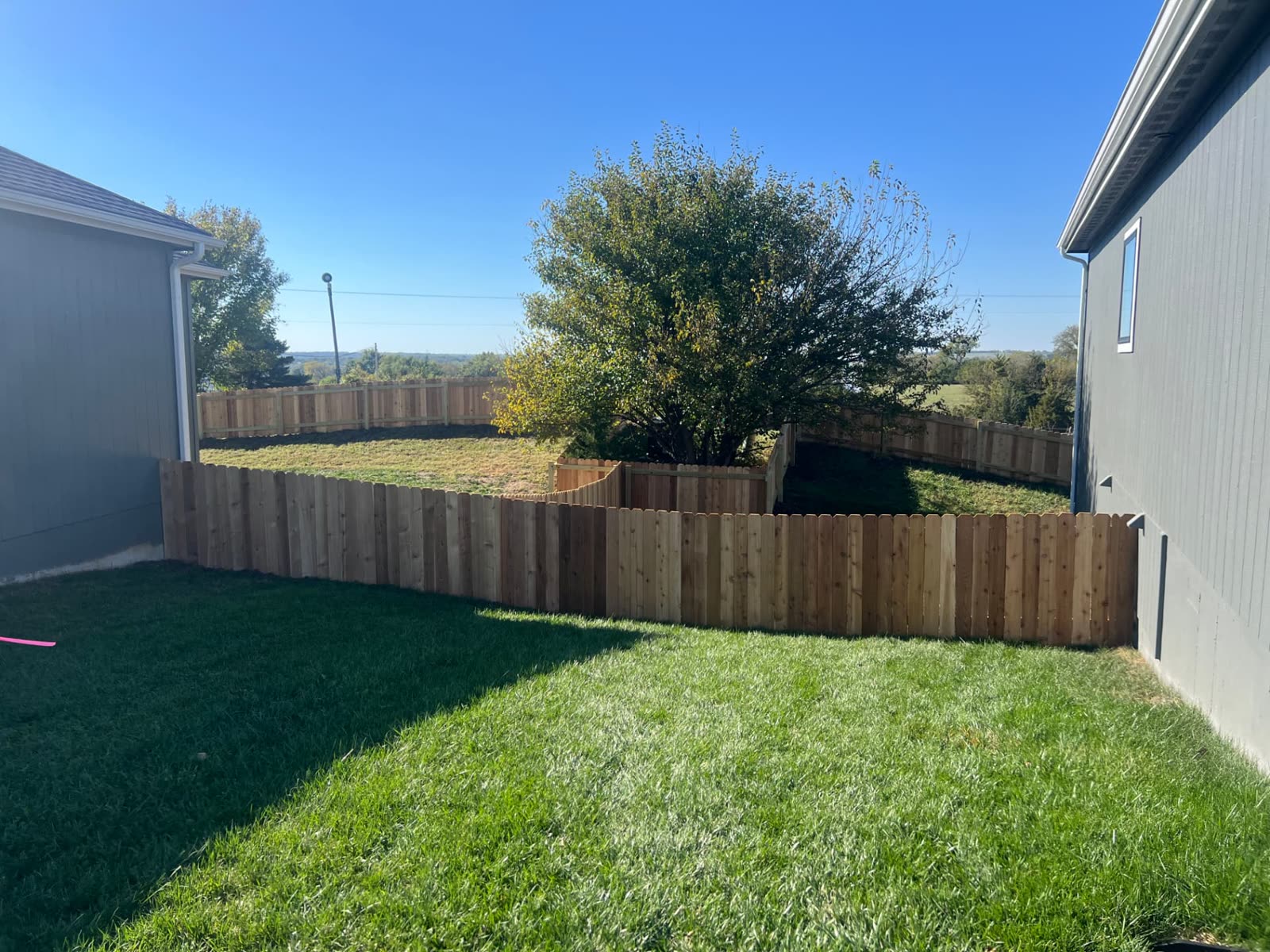 4 ft cedar dog-ear fence running between two gray homes with the fenced backyard beyond — Paola, KS