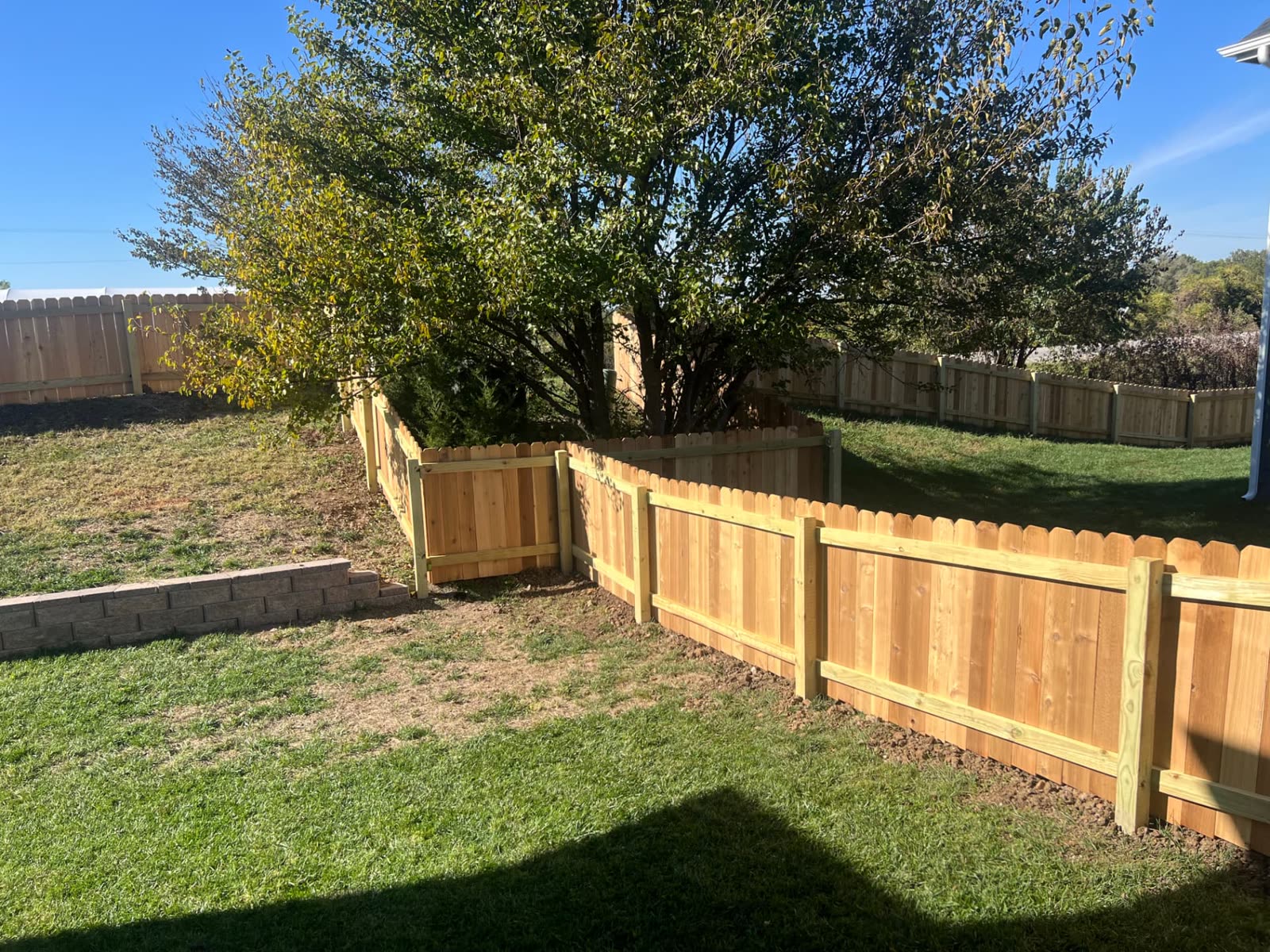 Back side of a 4 ft cedar fence showing treated posts and rails beside a block retaining wall — Paola, KS