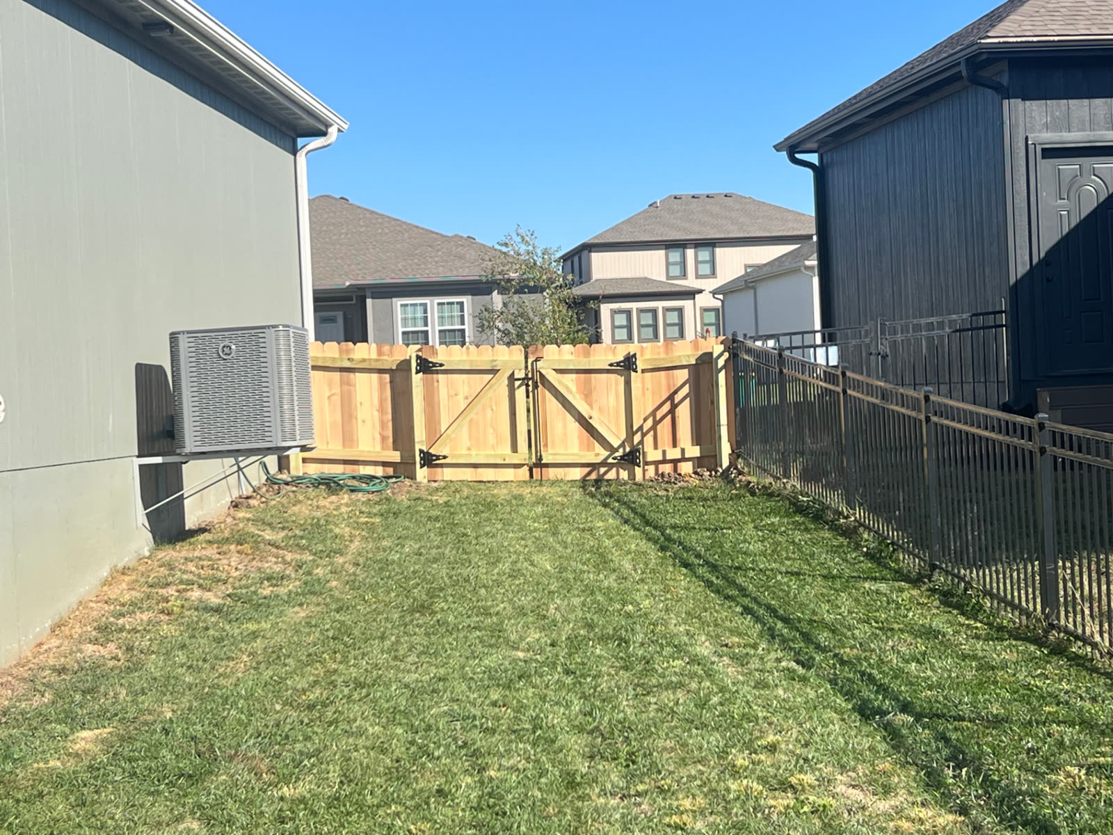 Cedar double gate with Z-brace frames and black strap hinges in a side yard between homes — Paola, KS