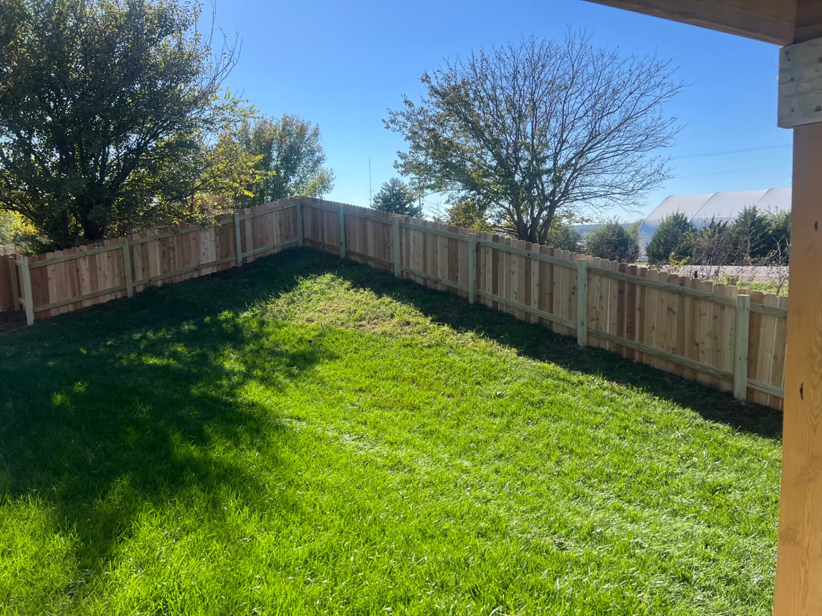 Back side of a 4 ft cedar dog-ear fence with treated posts and rails around a large grassy backyard — Paola, KS