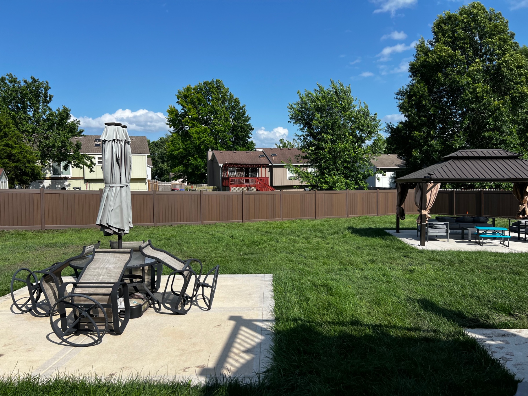 6 ft Woodland Select Chestnut brown vinyl privacy fence enclosing a sunny backyard with patio set and hardtop gazebo — Greenwood, MO