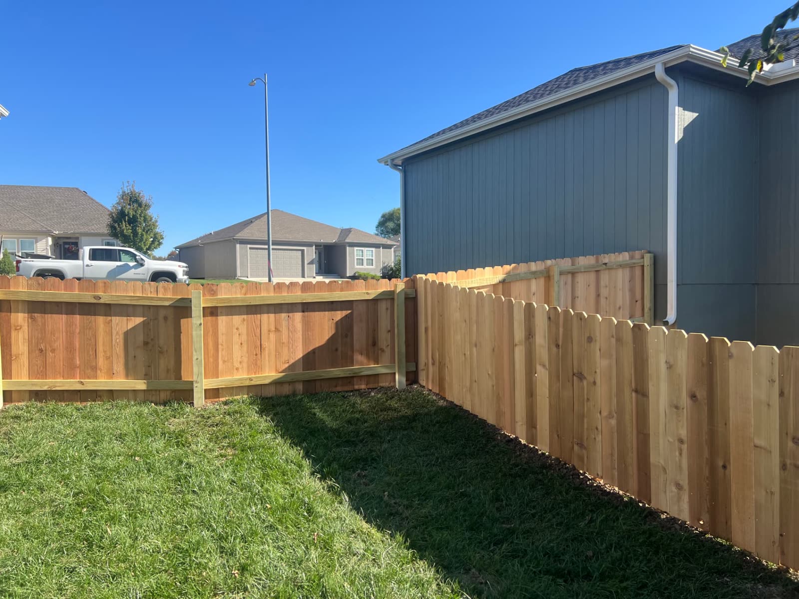 4 ft cedar dog-ear fence corner meeting the side of a gray house in a Paola, KS neighborhood
