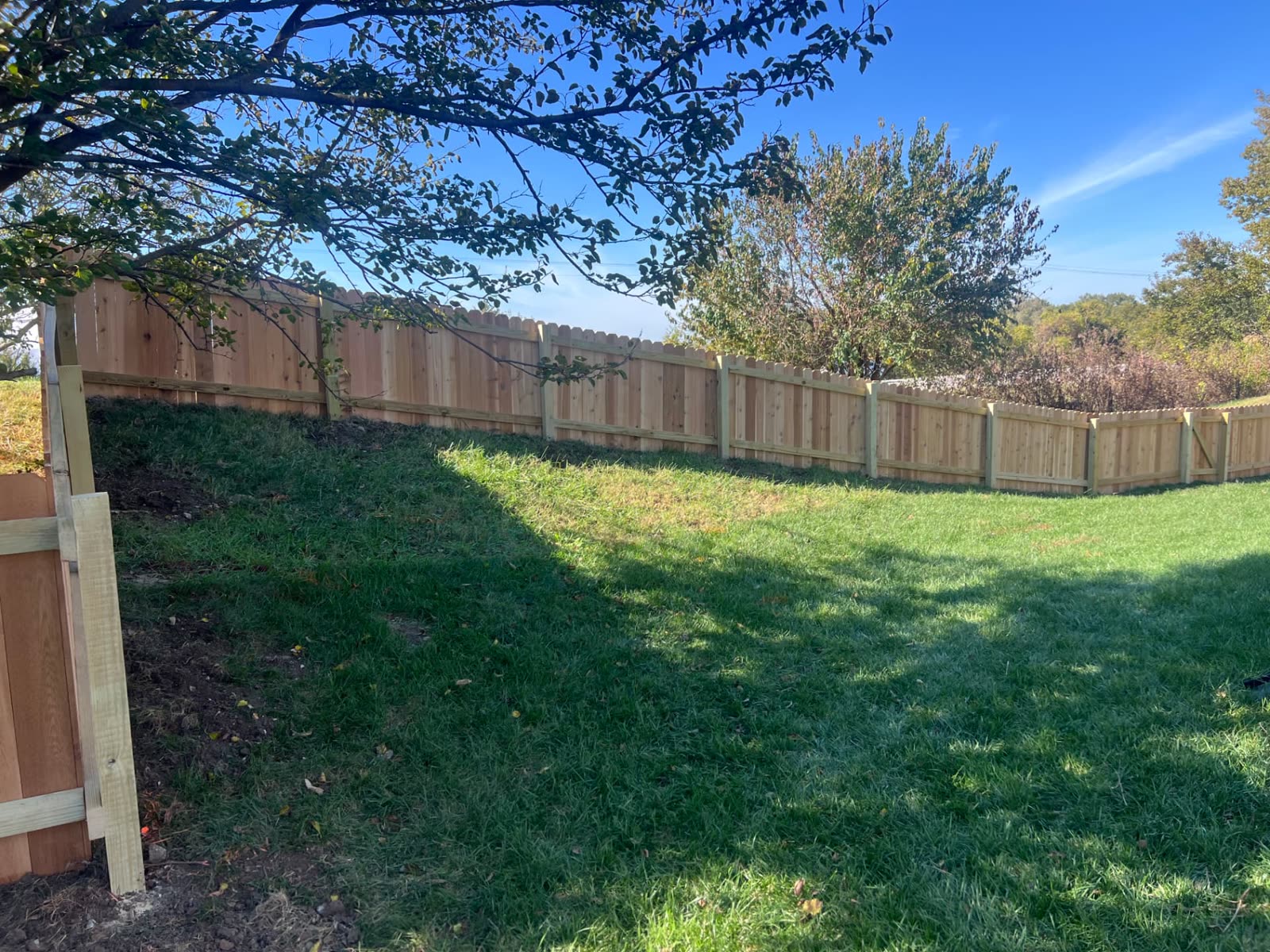 Long run of 4 ft cedar fence with treated posts and rails following a grassy hillside — Paola, KS